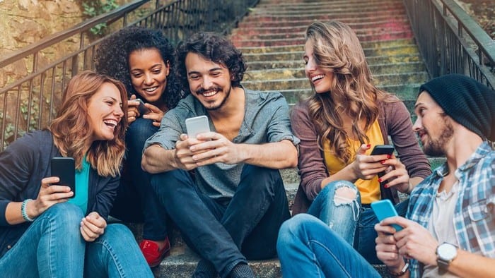 A group of young people smiling and watching TikTok on their mobile phones