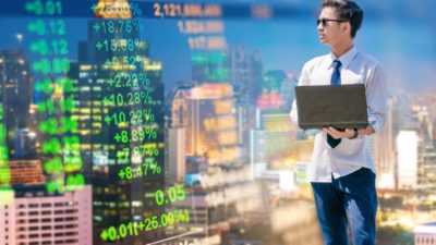 Young man with a laptop in hand watching stocks and trends on a digital chart.