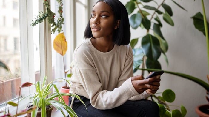 A woman looking through a window with an iPhone in her hand.