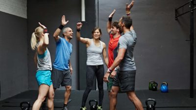 Group of people in a gym high five each other surrounded by gym equipment.