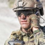 An Army soldier in combat uniform takes a phone call in the field.