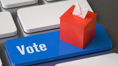 A square ballot box with an envelope going in it sits on a blue keyboard key that says 'vote'.