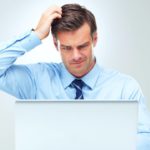 An ASX investor in a business shirt and tie looks at his computer screen and scratches his head with one hand wondering if he should buy ASX shares yet