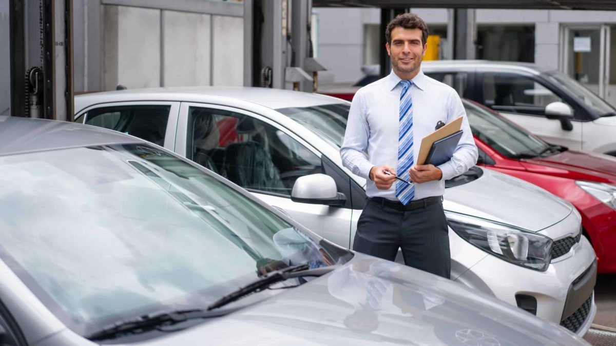 A car dealer stands amid a selection of cars parked in a showroom.