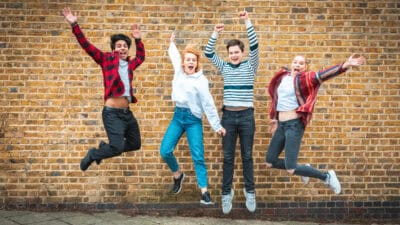 Happy teen friends jumping in front of a wall.