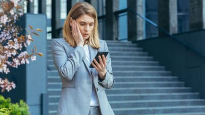 Frustrated and shocked business woman reading bad news online from phone.